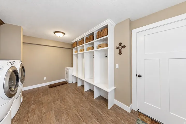 Wood-finish tile flooring, recessed ceiling light fixture, built-in white cabinetry with cubbies and upper shelving, and a solid-panel door with matte black hardware