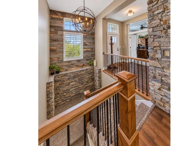 Stone accent wall with wood-finish flooring, staircase with wood handrail, and wrought iron balusters