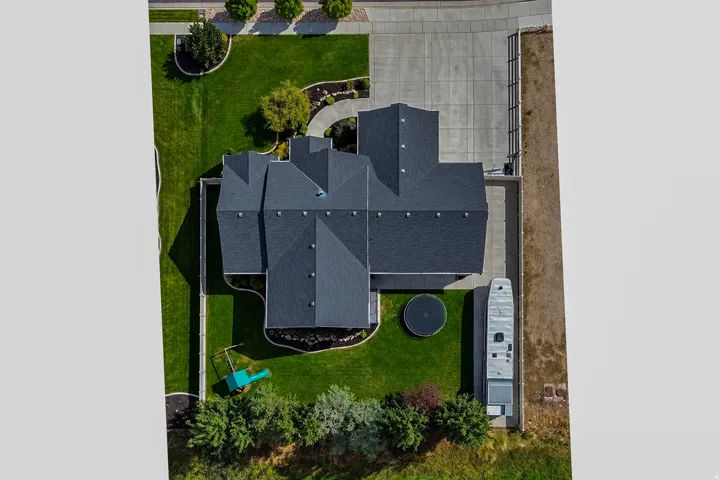 Manicured lawn, mature landscaping, expansive paved driveway, dark-toned shingle roof, and a structured property perimeter