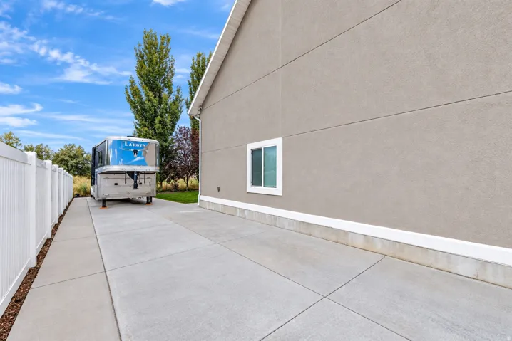 Stucco exterior with white trim, concrete driveway, and white privacy fencing