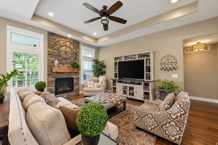 Living space featuring a stacked stone fireplace with a wood mantle, wood-finish flooring, and a tray ceiling with recessed lighting
