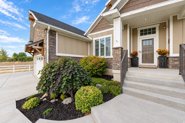 Craftsman-style exterior featuring stone accents, a wood-paneled entry door with transom window, concrete porch steps, and a landscaped garden bed