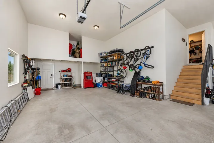 Spacious garage with concrete flooring, high ceilings, an integrated mezzanine level, wood stairs with metal railing, and multiple ceiling-mounted light fixtures