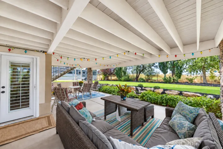 Covered patio with a painted beam ceiling, concrete flooring, and a glass-paneled door