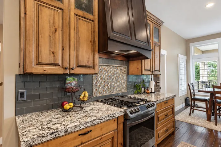 Hardwood flooring, natural wood cabinetry, granite countertops, tile backsplash, and built-in gas range
