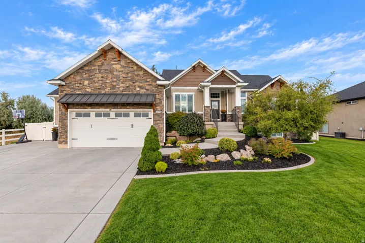 Stone and siding exterior with a dark shingle roof, concrete driveway, attached garage, and manicured landscaping