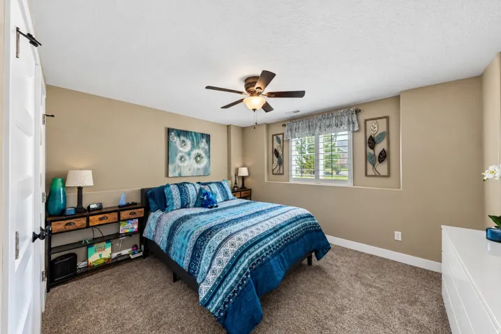 Carpeted bedroom featuring a ceiling fan, recessed window with plantation shutters, paneled interior door, and neutral wall tones