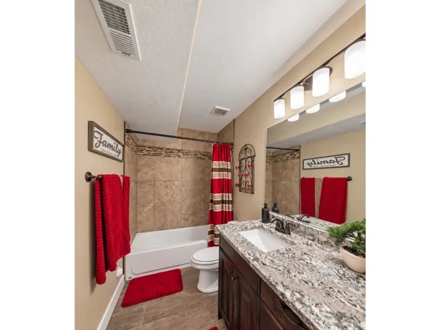 Bathroom featuring wood-finish flooring, a vanity with a light-colored countertop and integrated sink, a rectangular mirror, and a combined tub and shower with tiled surround
