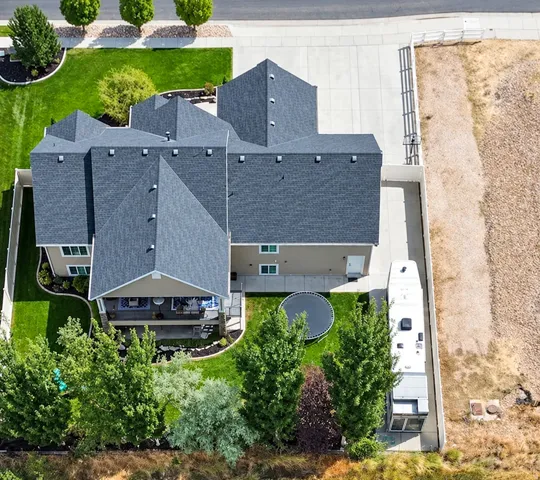 Expansive property featuring a large asphalt shingle roof, established landscaping, a concrete driveway, and a covered back patio