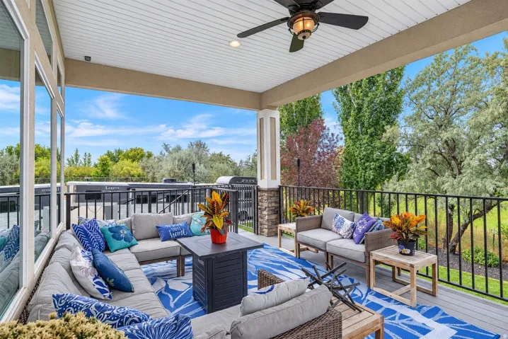 Expansive covered patio featuring a ceiling fan, stone-clad pillars, and a black metal railing