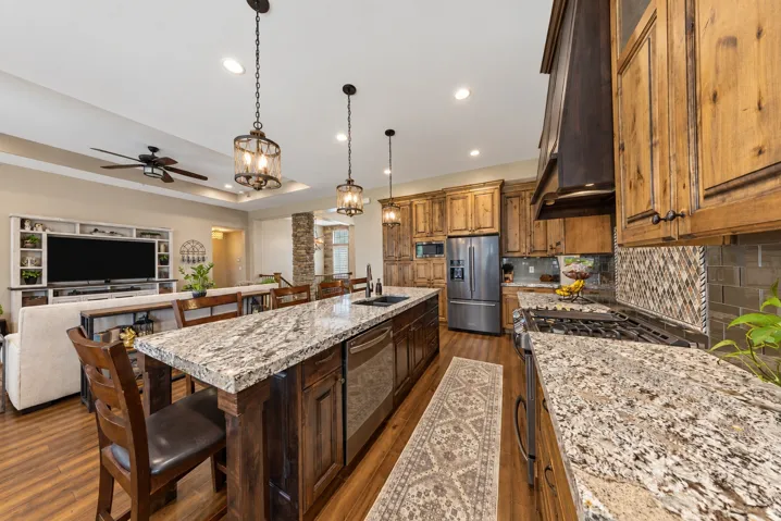 Kitchen featuring an expansive island with stone-finish countertops, stainless steel appliances, wood-finish cabinetry, and a tile backsplash