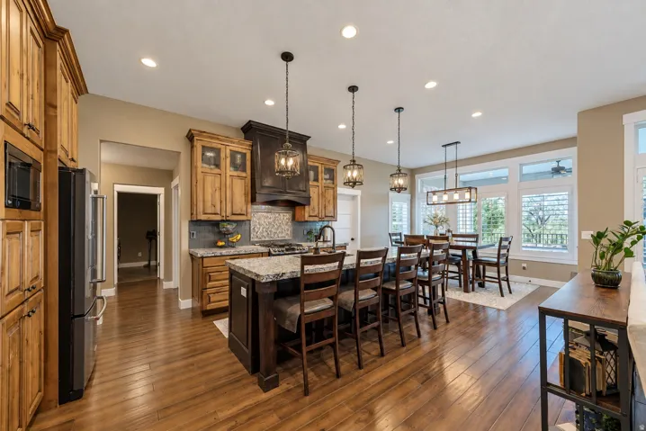 Hardwood flooring, recessed lighting, kitchen island with seating, stainless steel appliances, and abundant natural light from multiple windows