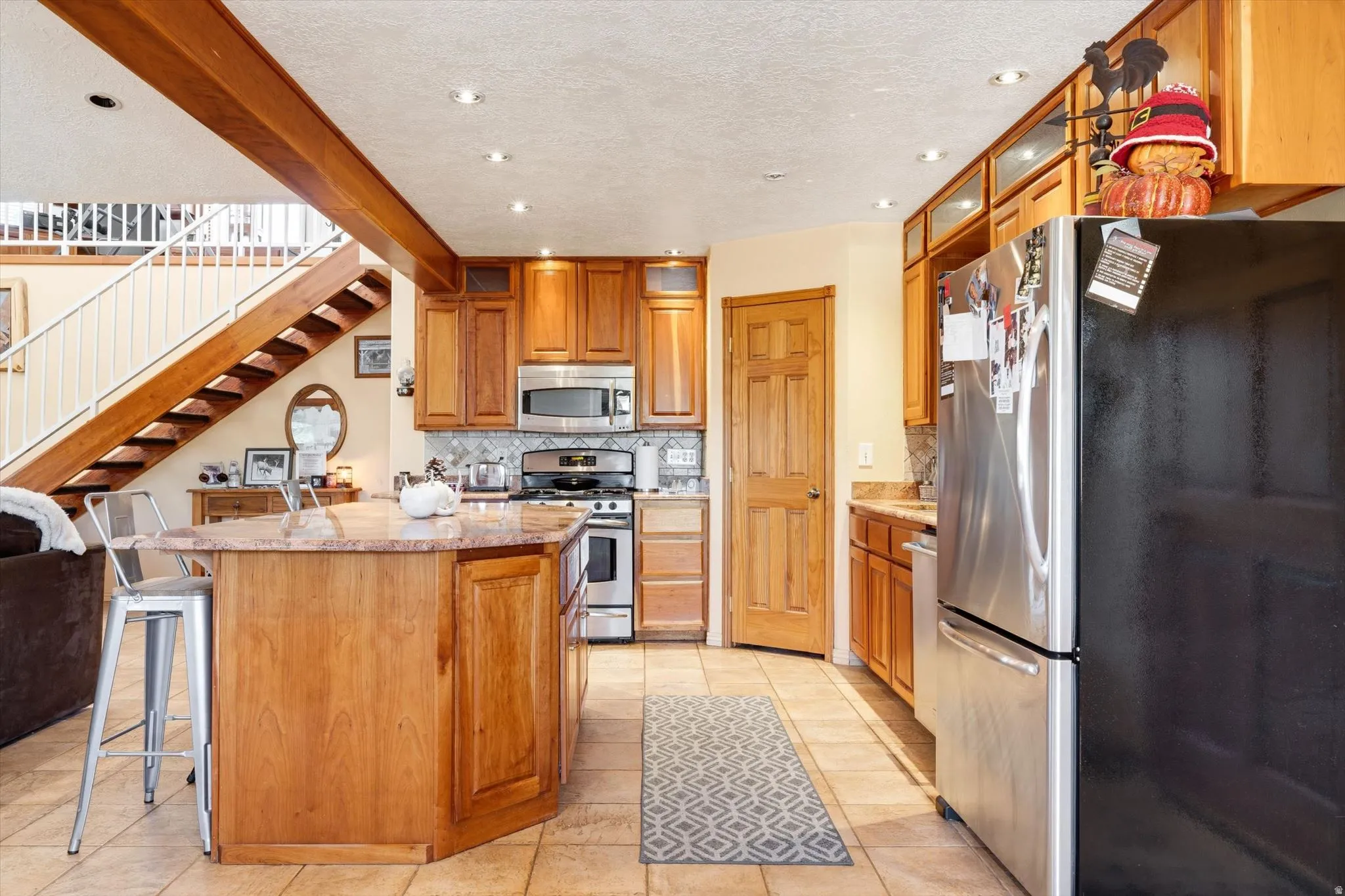 Kitchen featuring wood cabinetry, stainless steel appliances, a center island with countertop seating, recessed lighting, and tile flooring