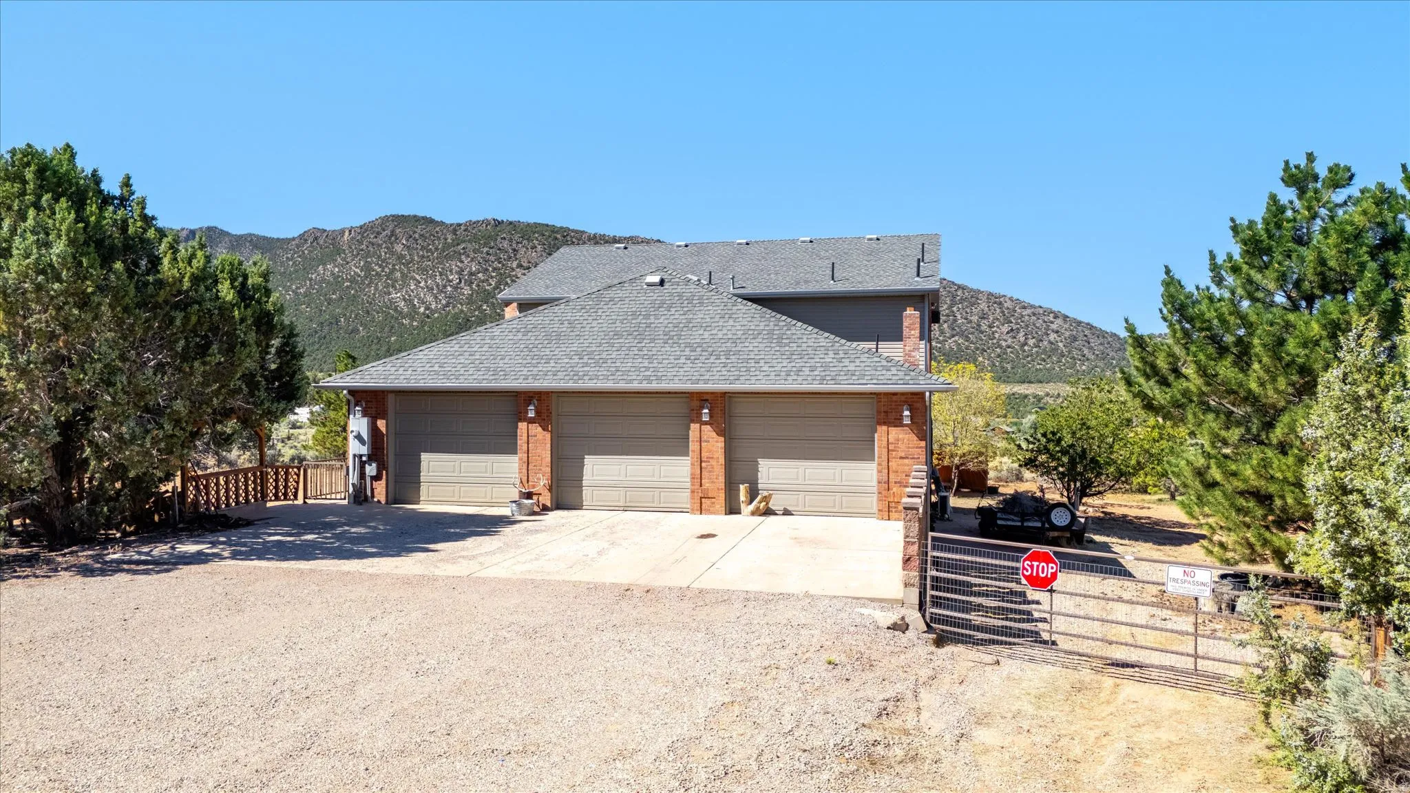 Brick facade residence with a three-car garage, gravel driveway, and a gated entry