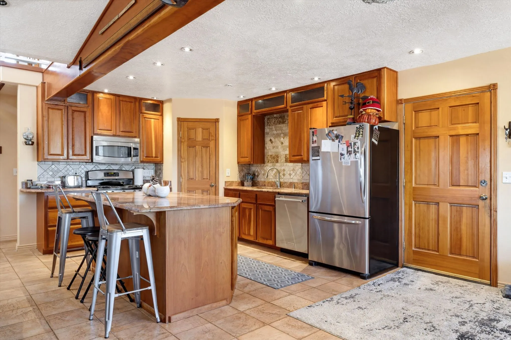 Kitchen featuring wood cabinetry, stainless steel appliances, a center island with a stone-finish countertop, and tile flooring