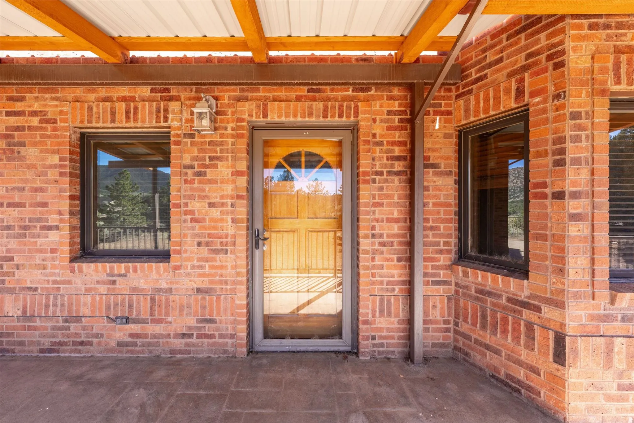 Brick exterior with a covered patio, exposed wood beams, and a wood-panelled entry door