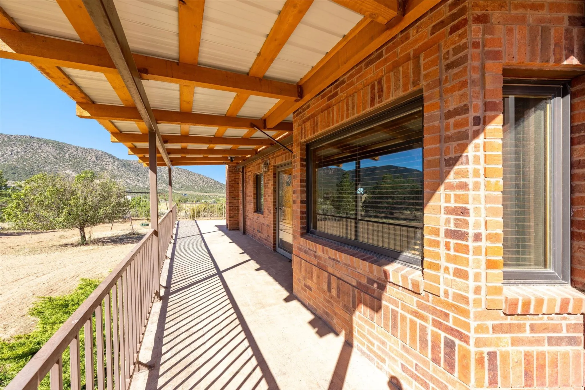 Brick exterior featuring a covered porch with a metal roof and wooden beams, framed by a metal railing