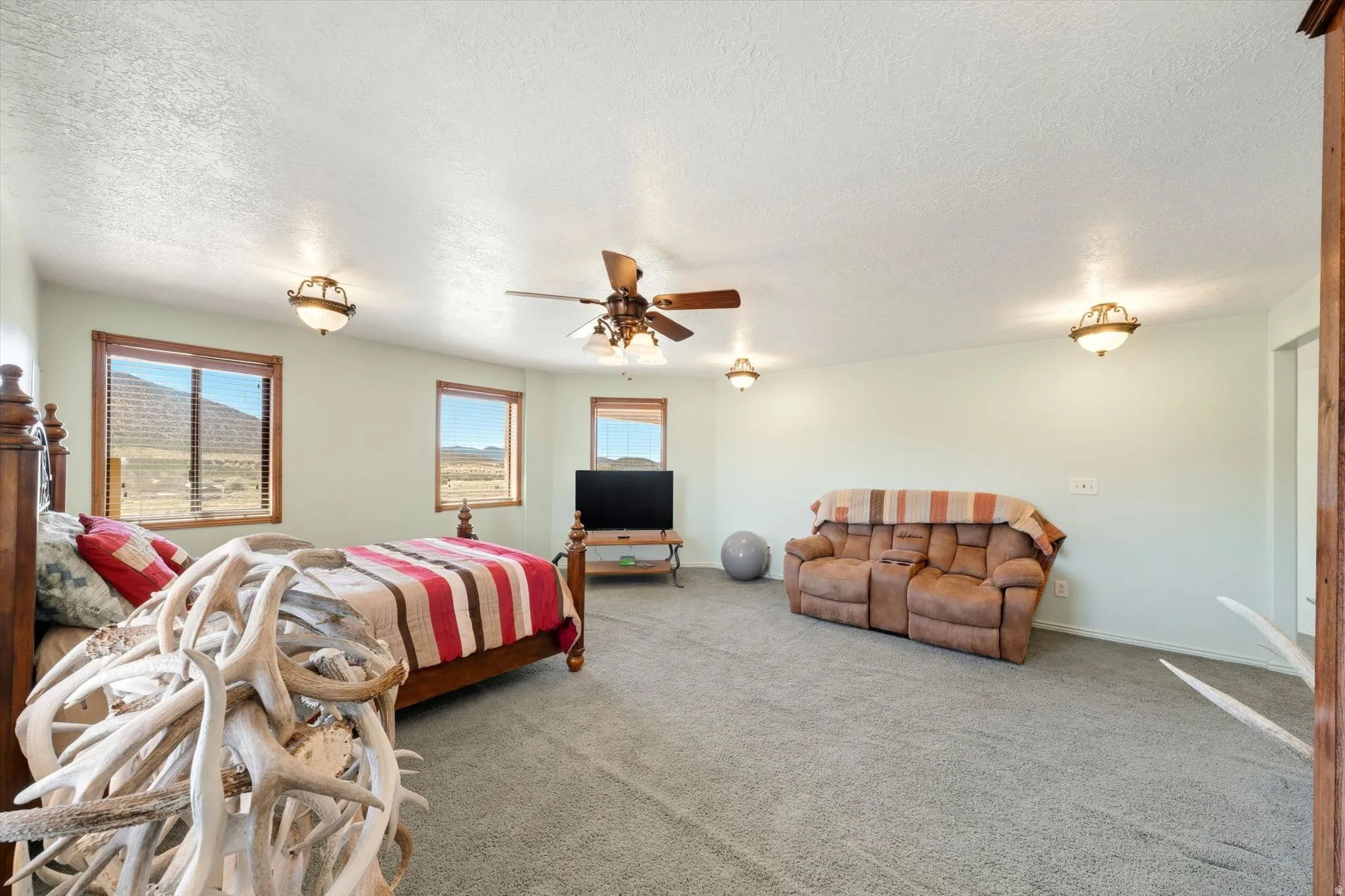 Wall-to-wall carpeting, multiple windows with wood trim, ceiling fan with integrated lighting, and additional flush-mount lighting fixtures