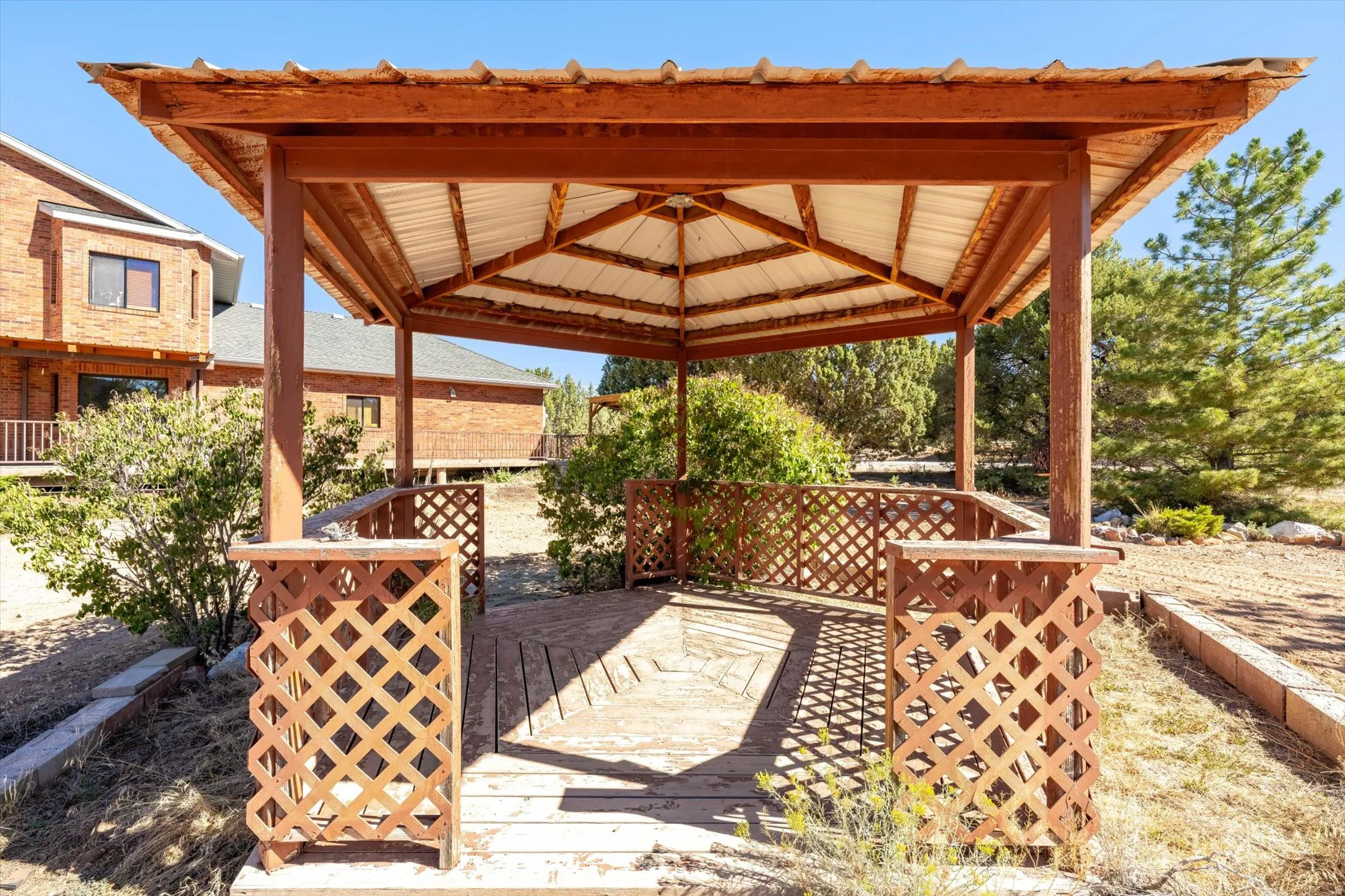 Wood-frame gazebo with a corrugated metal roof and lattice railing, featuring an elevated wood-plank floor