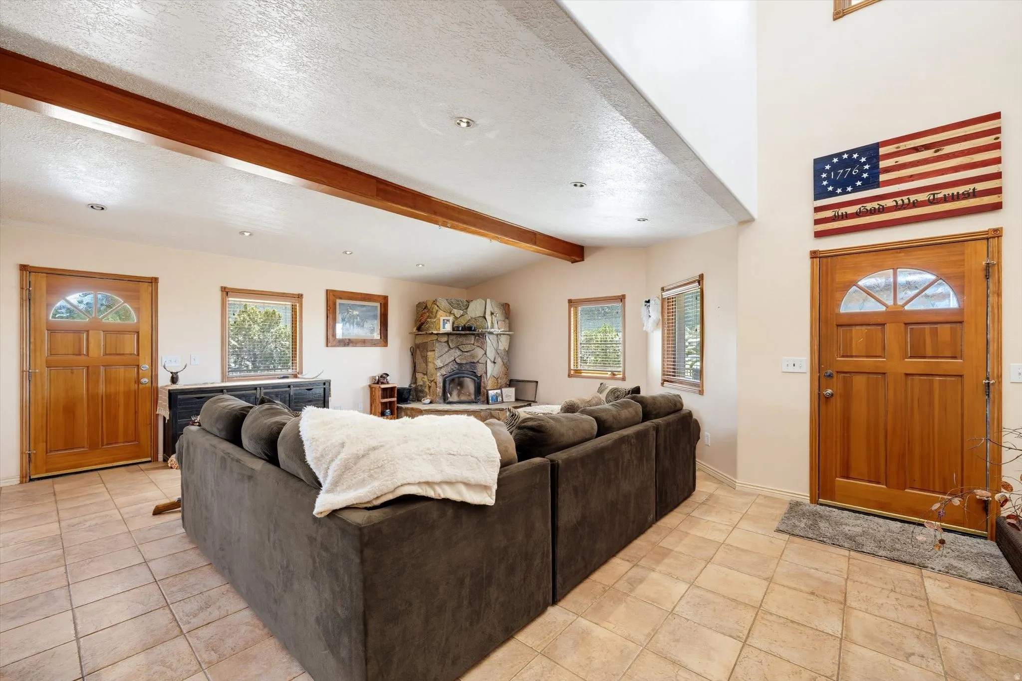 Ceramic tile flooring, exposed wood beam, recessed lighting, stone fireplace, and wood-framed windows