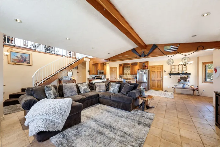 Recessed lighting, wood-beam ceiling, tile flooring, open-concept design, and a visible kitchen area with stainless steel appliances