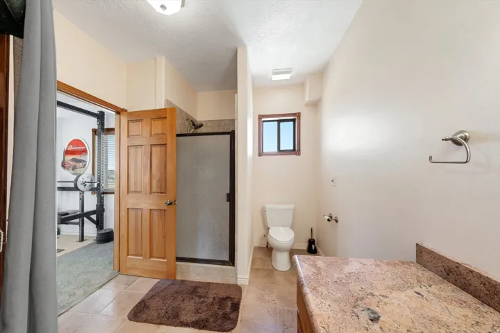 Bathroom with a single vanity featuring a stone countertop, a toilet, a shower with a framed glass enclosure, and a wood-framed window