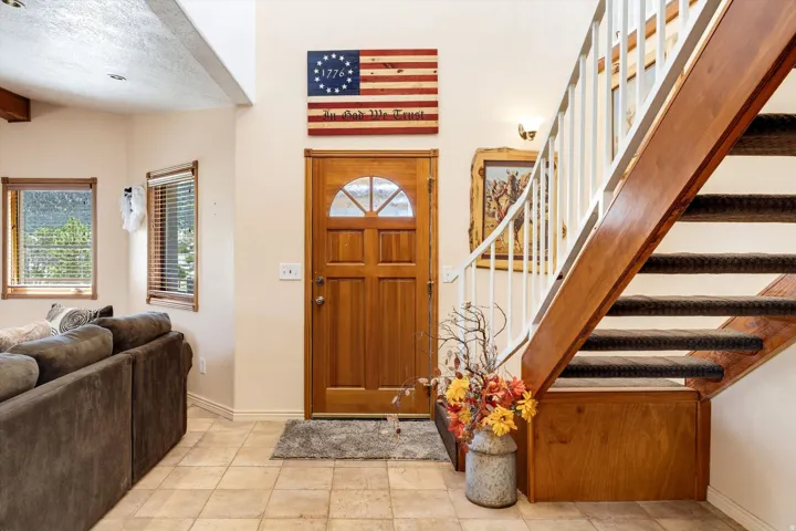Wood-finish entry door with arched lites, tile flooring, wood-finish staircase with carpeted treads, and multiple windows with wood-finish trim