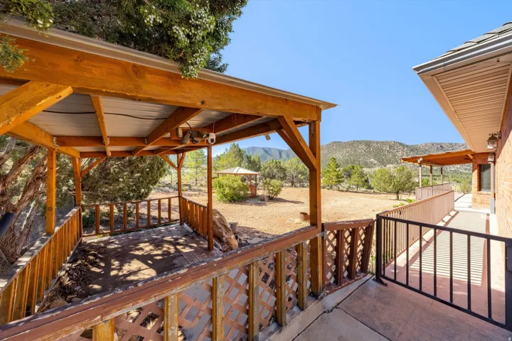 Covered wooden patio with slatted railing, exterior brick siding, an extended concrete pathway, and a distant mountain backdrop
