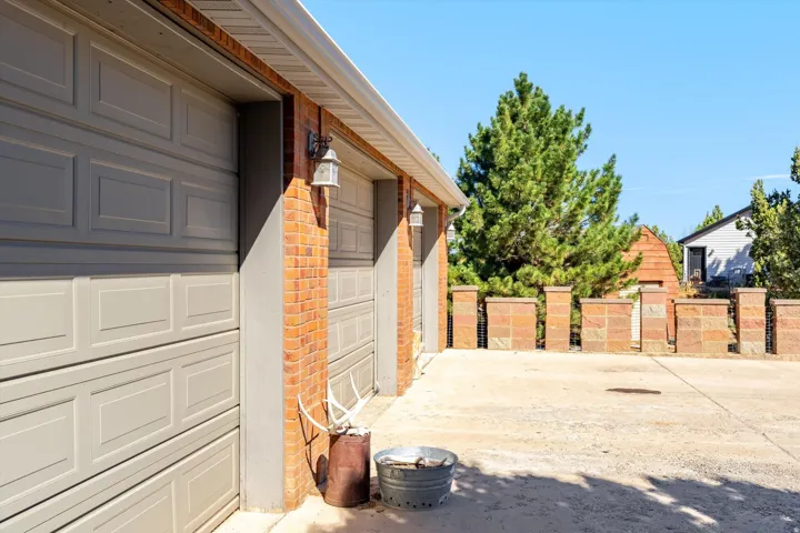 Attached two-car garage with panel doors, brick siding, exterior wall lanterns, and a concrete driveway