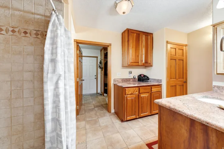 Tile flooring, wood cabinetry, stone countertops, tiled shower surround with decorative accent band, and recessed sink
