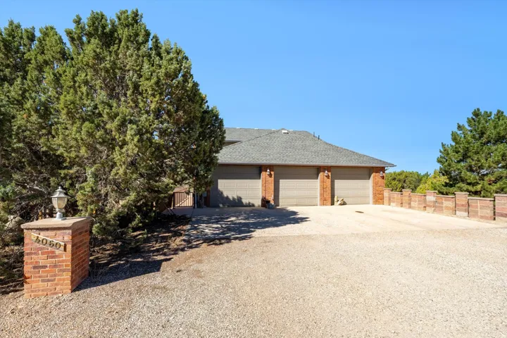 Gravel driveway with extensive parking, two-car garage with brick accents, and a brick-clad address pillar