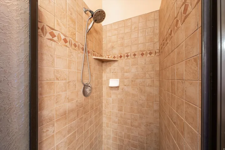 Tiled shower enclosure featuring a decorative accent band, built-in corner shelf, and handheld shower fixture