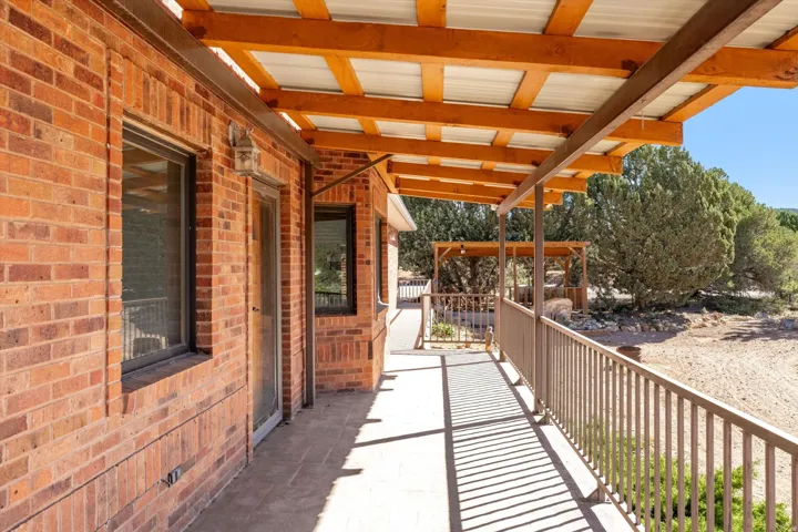Brick exterior with a covered porch featuring exposed wood beams, a corrugated roof, and a metal railing