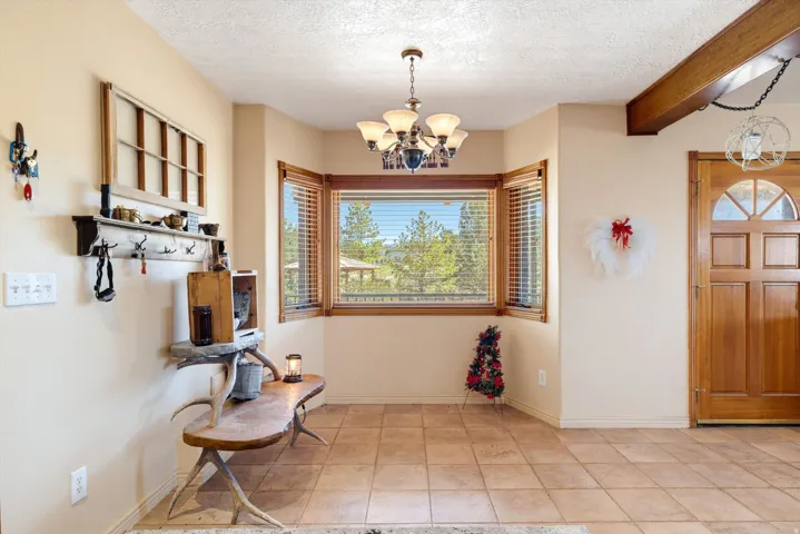 Tiled flooring, bay window with wood-finish blinds, wood-paneled entry door, wood beam ceiling accent, and a chandelier with frosted glass shades