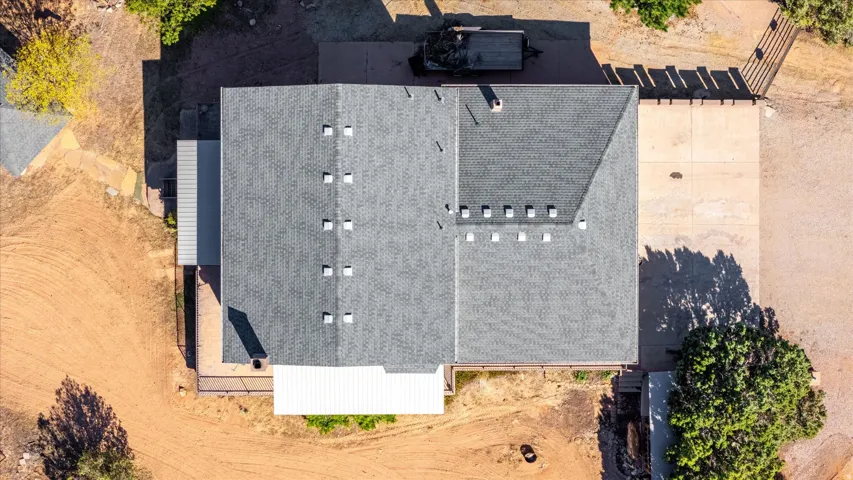 Asphalt shingle roof with multiple skylights, expansive concrete paving, and a covered patio area