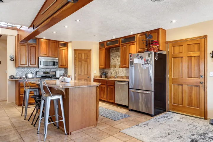 Kitchen featuring wood cabinetry, stainless steel appliances, a center island with a stone-finish countertop, and tile flooring