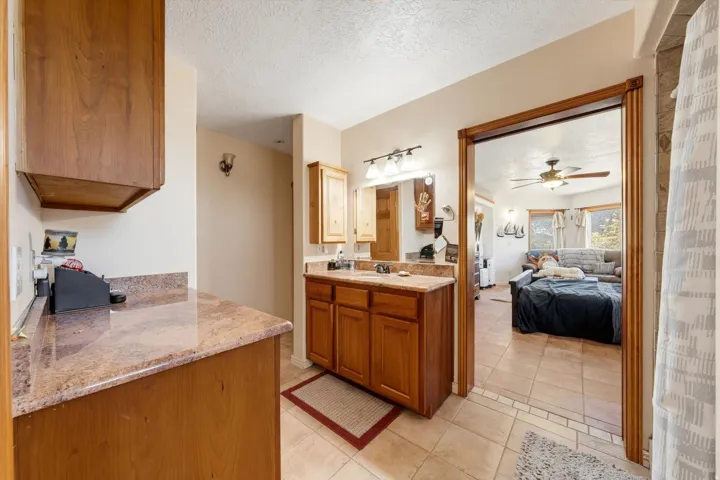 Wood-finish cabinetry with stone-finish countertops, ceramic tile flooring, and integrated vanity lighting