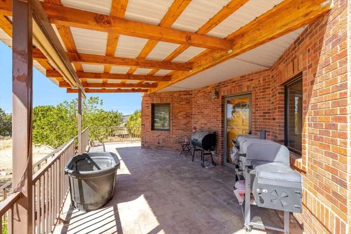 Covered patio featuring a wood beam and corrugated metal roof, brick exterior, stamped concrete flooring, and metal railings