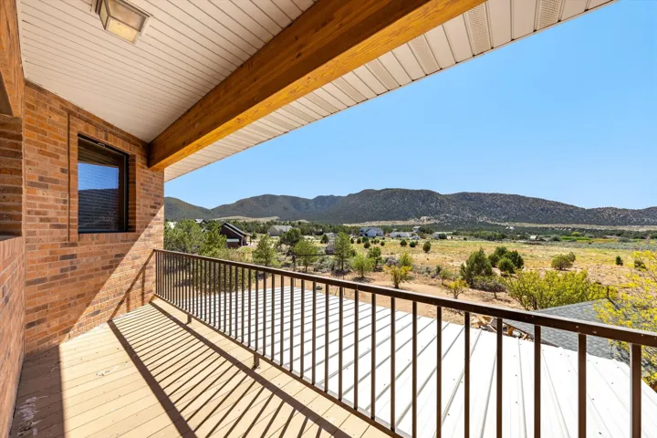 Covered patio featuring wood-finish flooring, a brick exterior wall, and metal railing