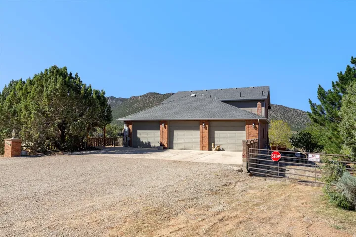 Brick exterior with three garage bays, a gravel driveway, and a gated entry