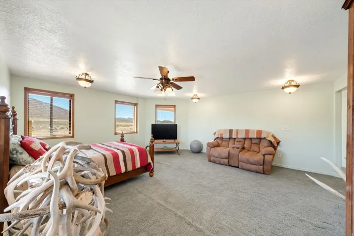 Wall-to-wall carpeting, multiple windows with wood trim, ceiling fan with integrated lighting, and additional flush-mount lighting fixtures