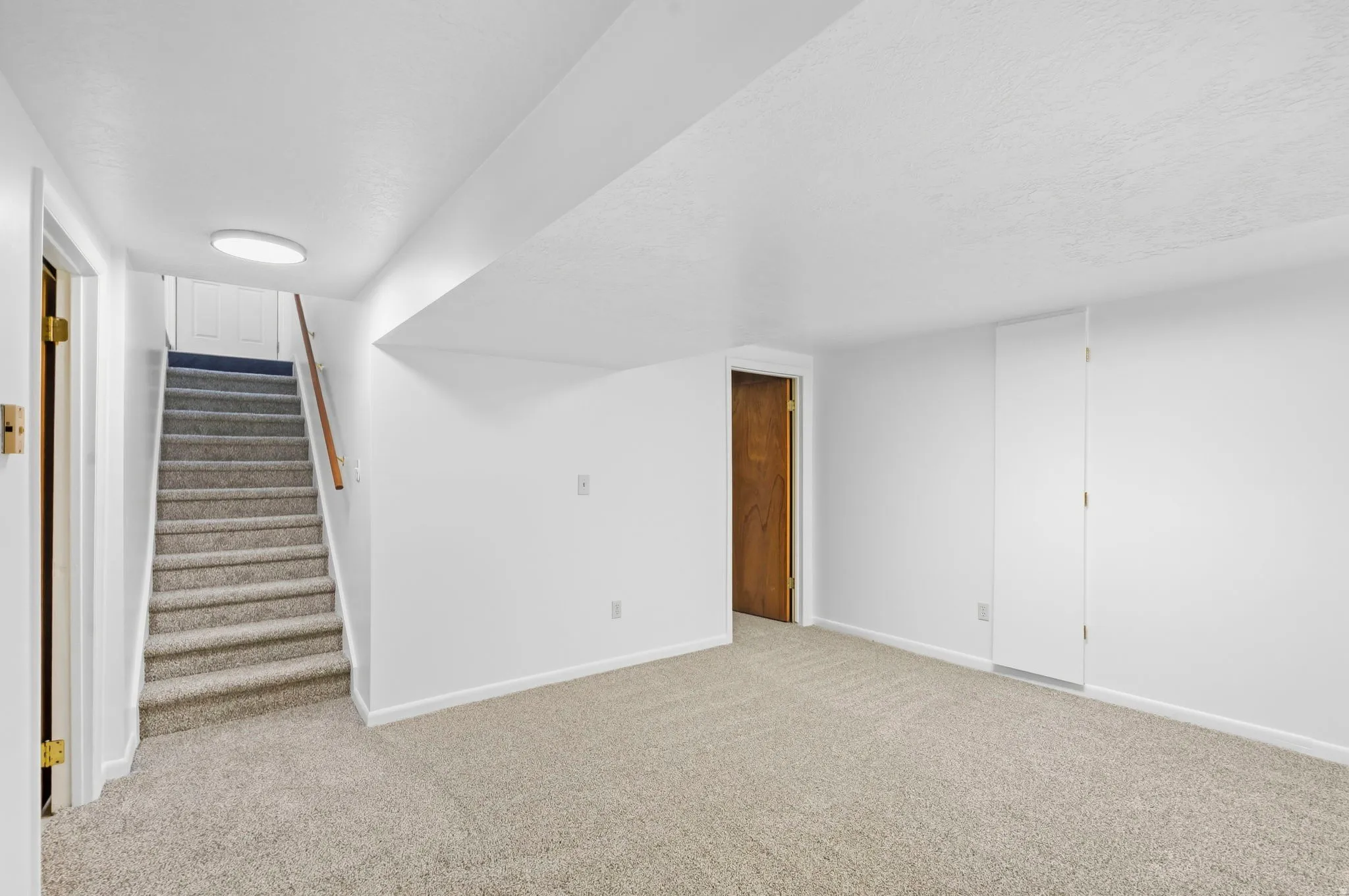 Carpeted flooring extending into a carpeted staircase with a wood handrail, white walls, and a recessed ceiling light