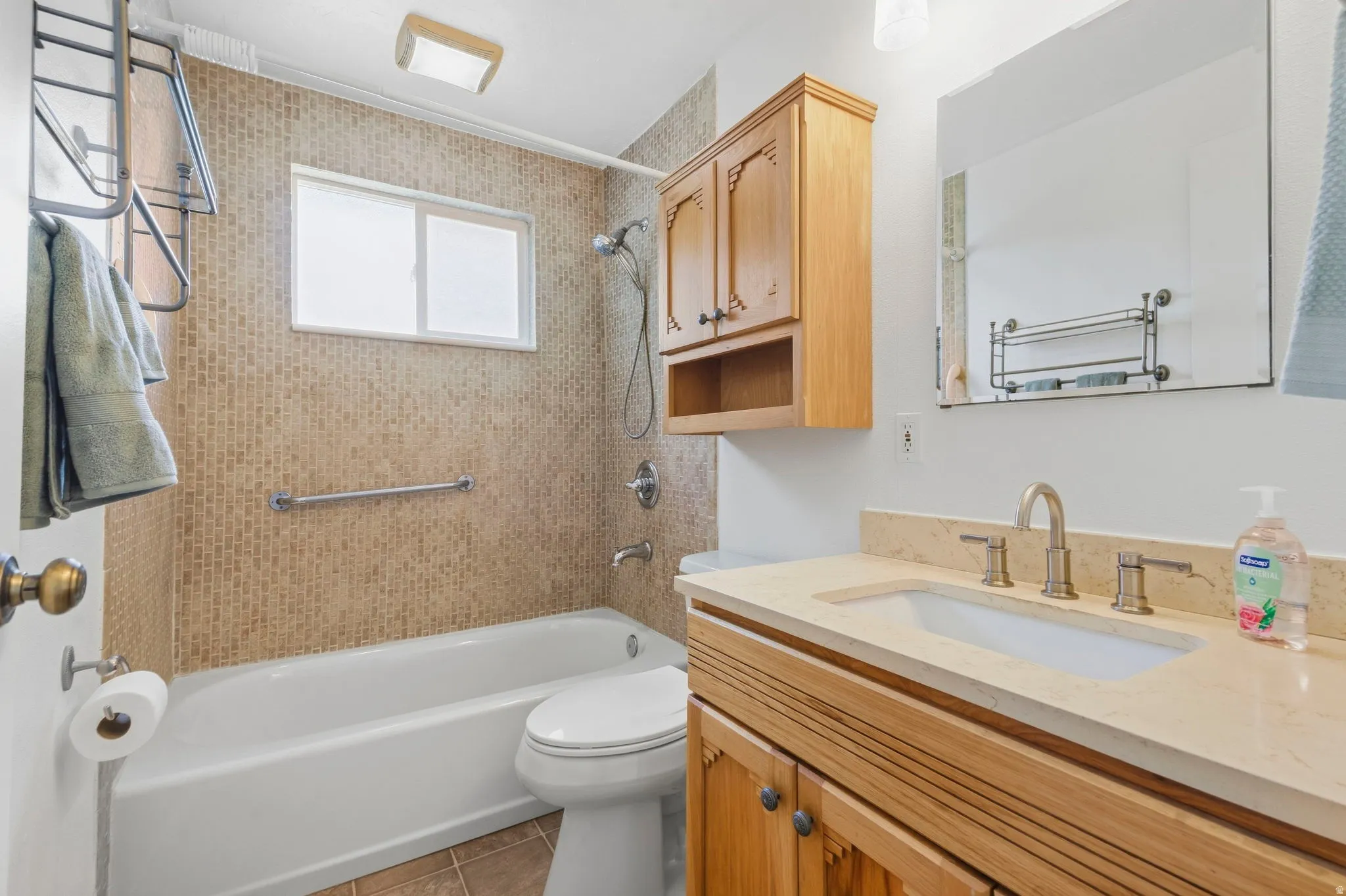 Bathtub and shower combination with a textured tile surround, window, and grab bar