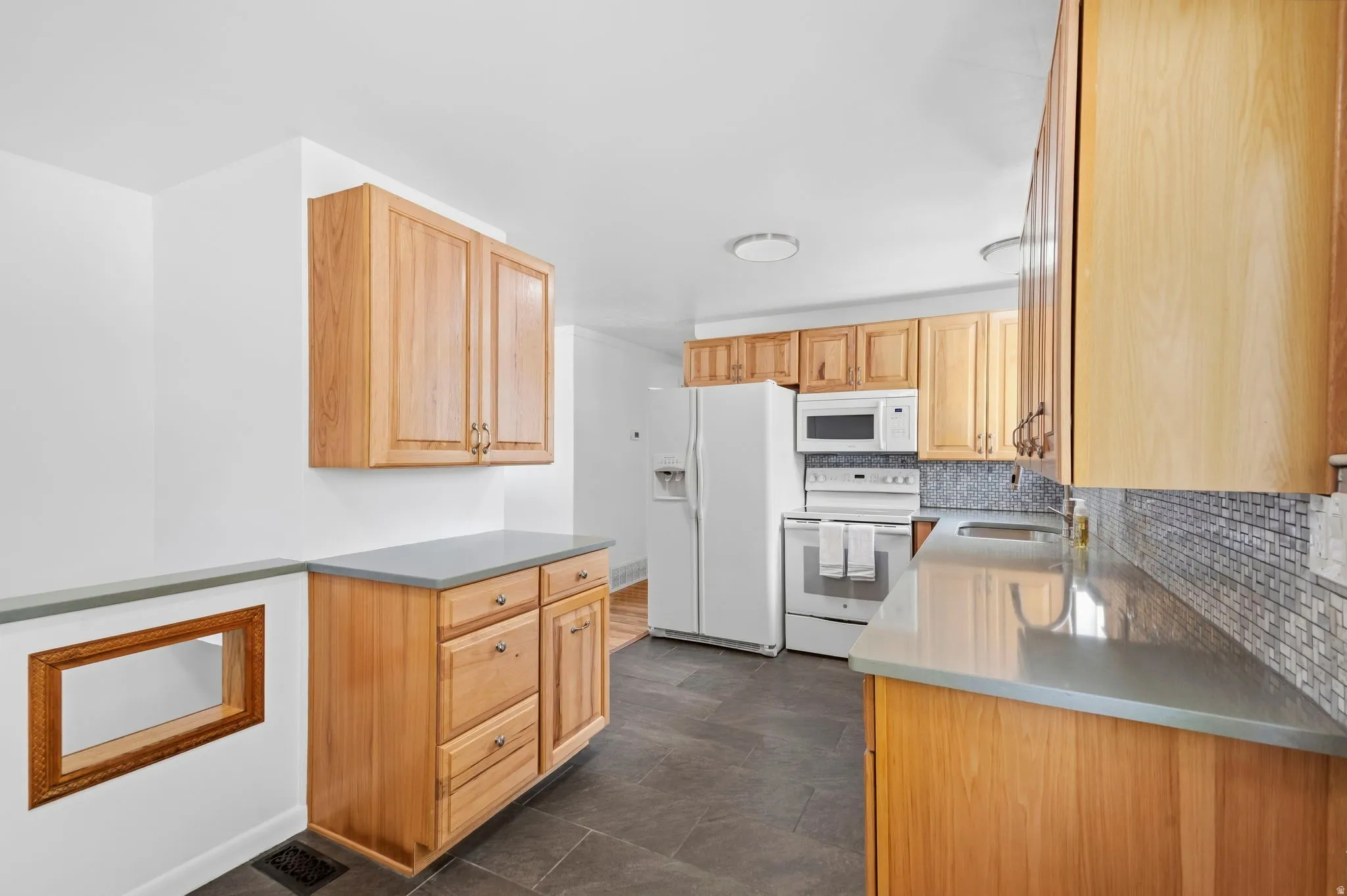 Kitchen featuring wood cabinetry, light countertops, a tile backsplash, dark floor tiling, and white appliances