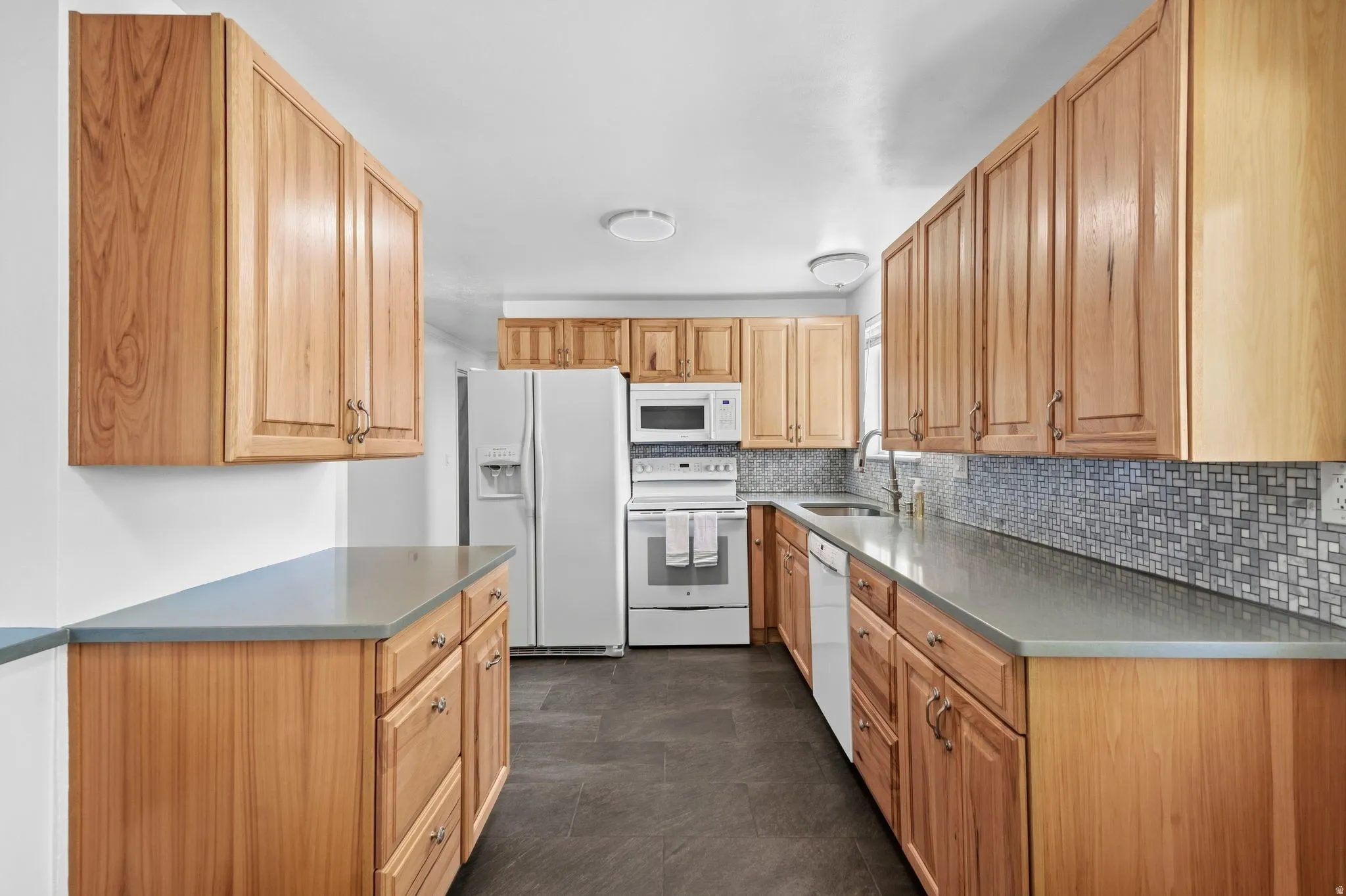 Full kitchen featuring wood-finish cabinetry, light grey countertops, and a mosaic tile backsplash