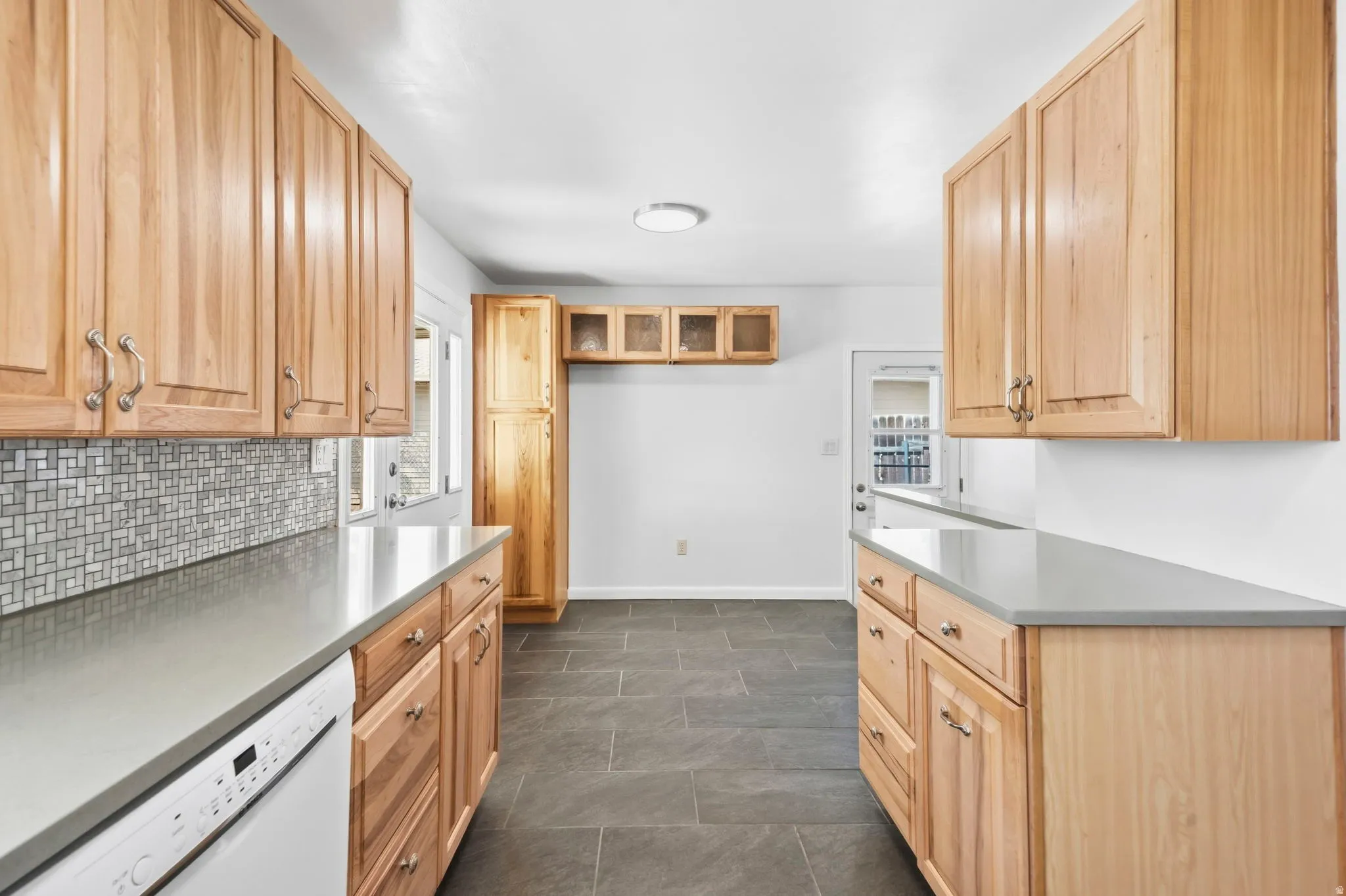 Wood cabinetry, light-toned countertops, and mosaic tile backsplash