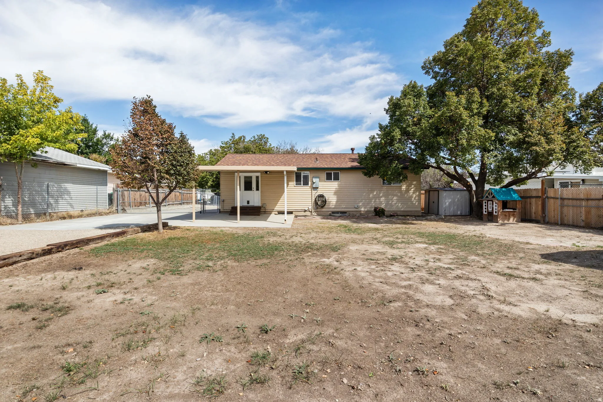 Expansive backyard featuring a covered patio, mature trees, and a gravel driveway