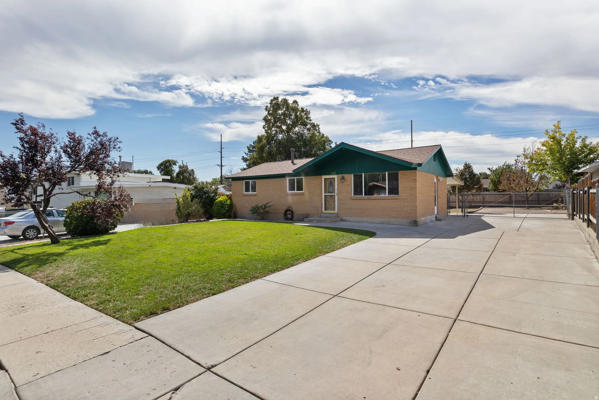 Brick exterior with a dark green roof trim, featuring a concrete driveway, a sidewalk, and a manicured lawn
