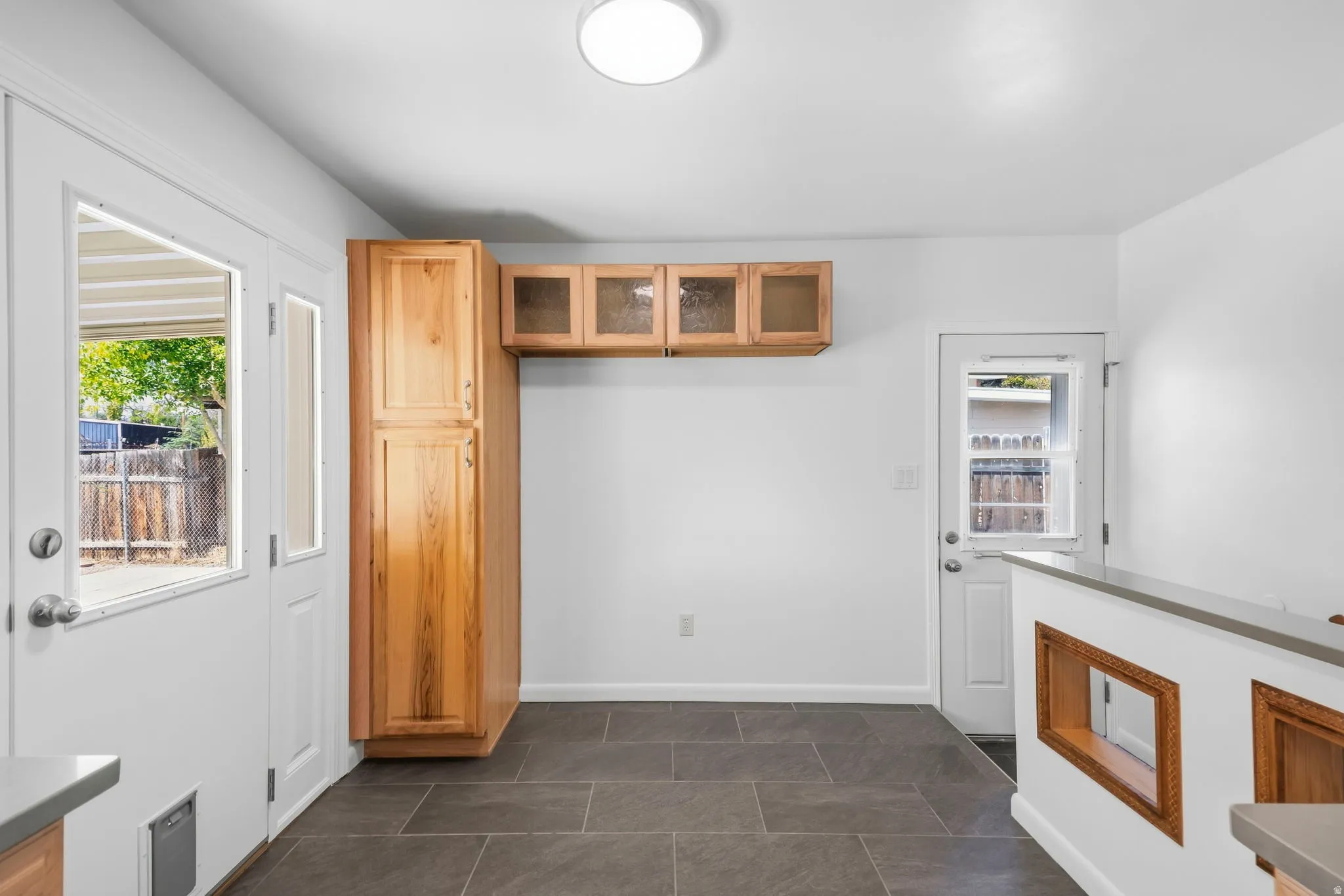 Slate-finish tile flooring, natural wood cabinetry with glass-front uppers, and a peninsula with a composite countertop