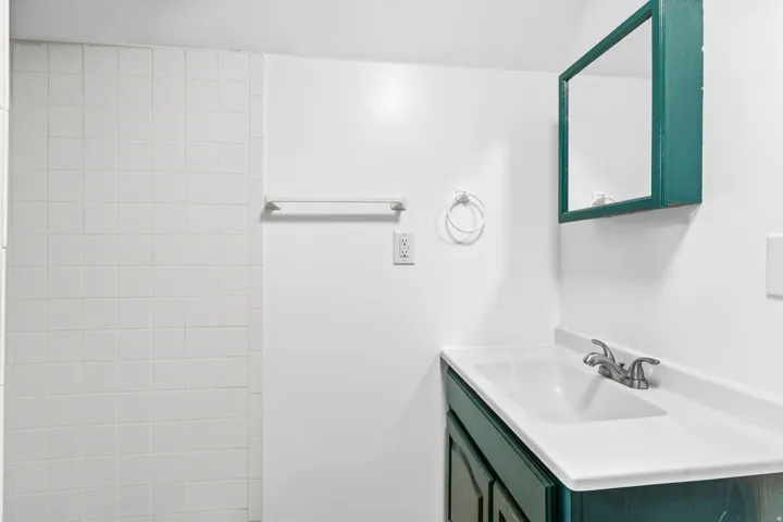 White tiled wall, dual-handle faucet, integrated sink, built-in vanity cabinet, wall-mounted mirrored medicine cabinet